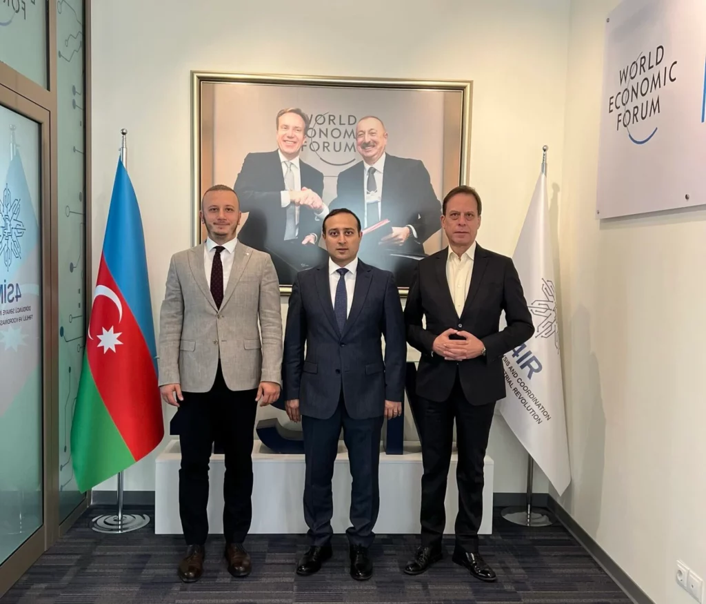 Three men in suits standing in front of a wall with flags.