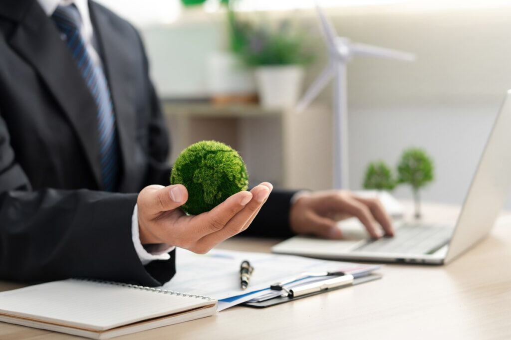 A man in a suit holding a small tree in front of a laptop.