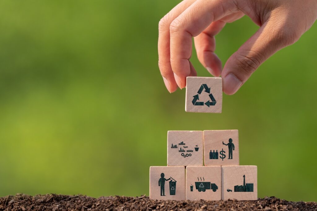 A hand is holding wooden blocks with recycling icons on them.