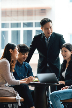 A diverse group of four professionals collaboratively working around a laptop at a modern office table.